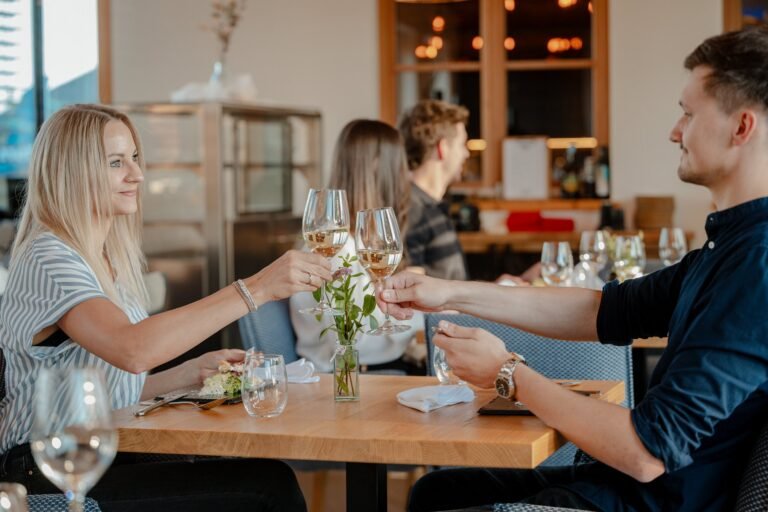Vier Gäste stoßen mit Weißwein am Tisch an
