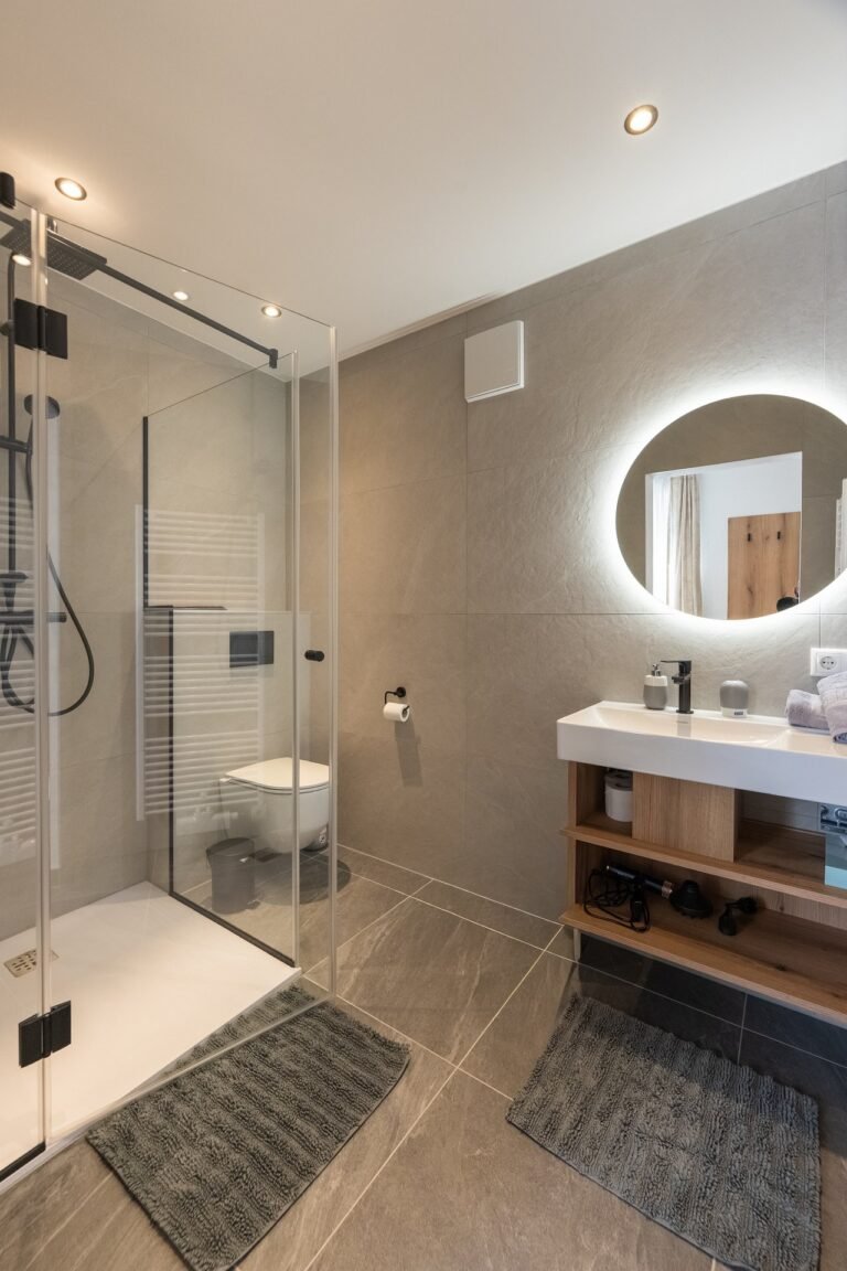 Badezimmer mit beleuchtetem Rundspiegel, Waschtisch und Dusche