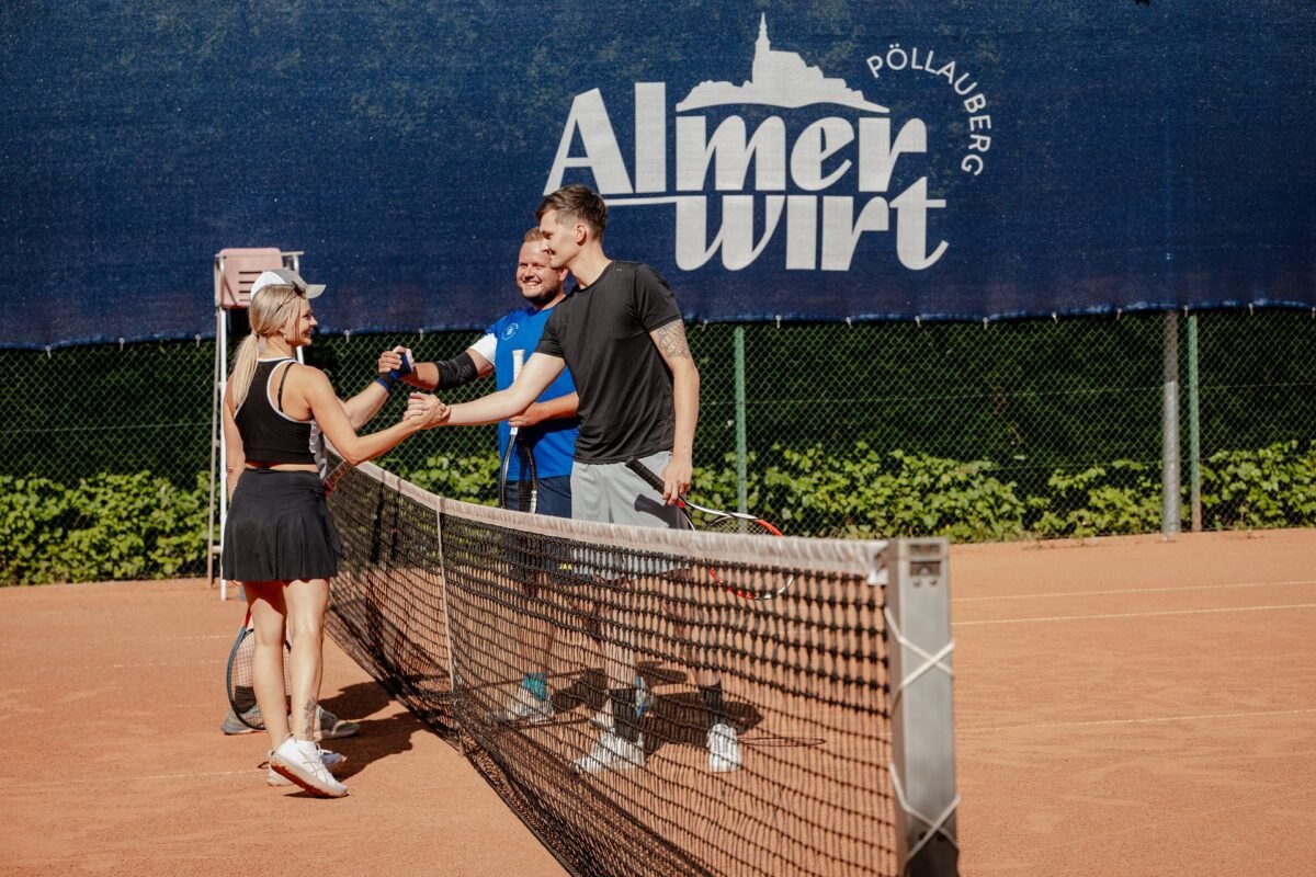 Drei Tennisspielende geben sich am Netz die Hand, dahinter die Almerwirt-Bande