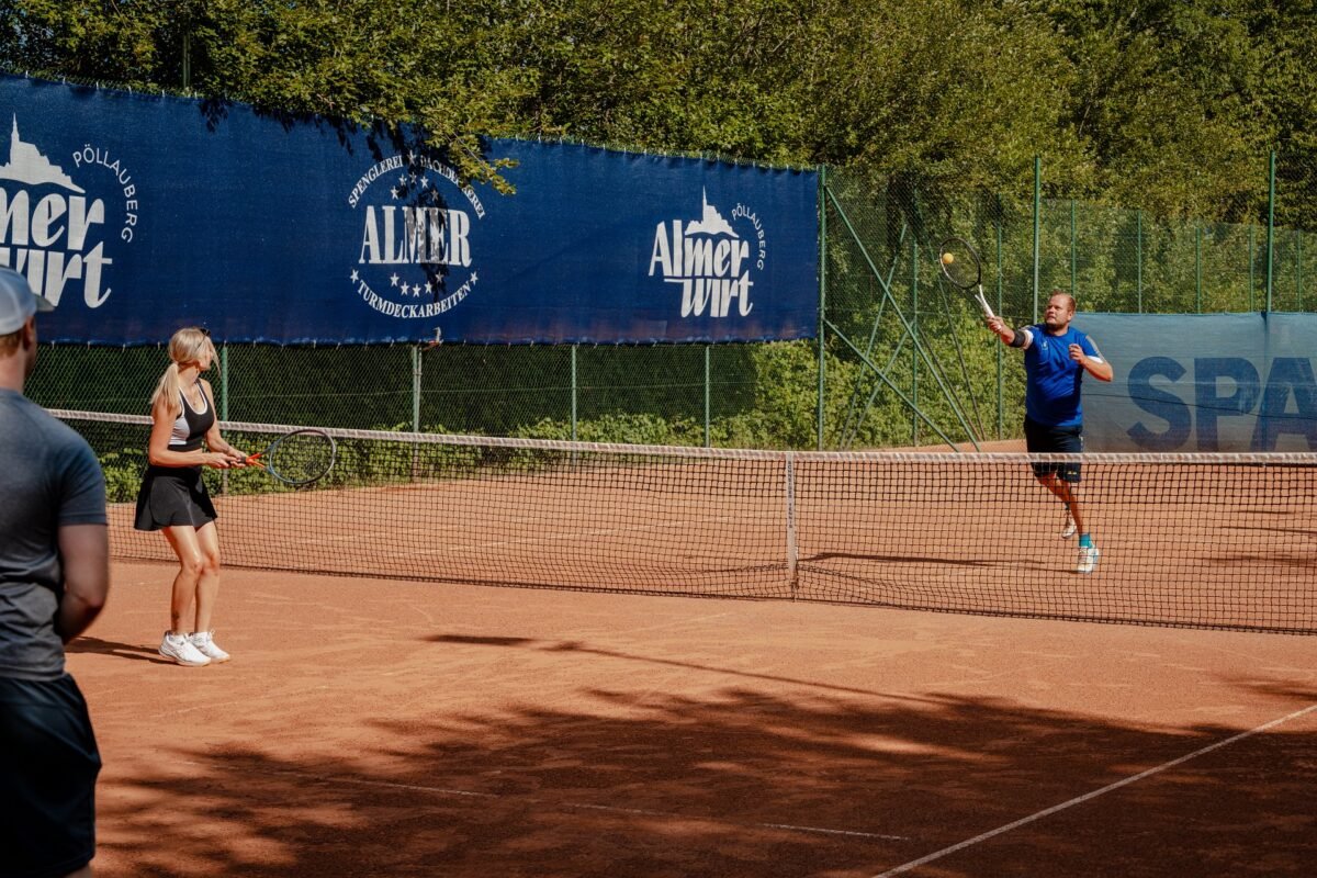 Zwei Personen beim Tennisspiel auf dem Sandplatz beim Almerwirt