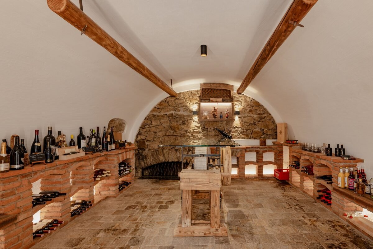 Gewölbter Weinkeller mit Natursteinwand, Weinregalen und Verkostungstisch